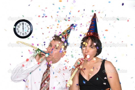 Couple celebrates a happy New Years Eve occassion by wearing party hats and blowing horns under falling confetti