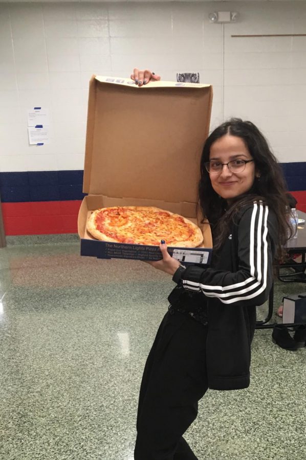 Dakshina stands holding a pizza, almost if asking, You wanna pizza this. 